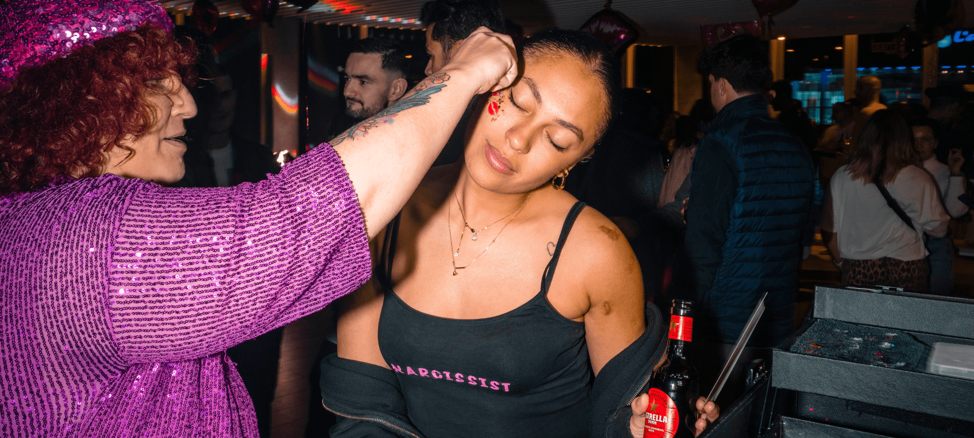 Professional makeup artist applying one of her designs on a young woman during the Love Crew Party